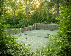 an outdoor tennis court surrounded by trees and bushes with the sun shining through the trees