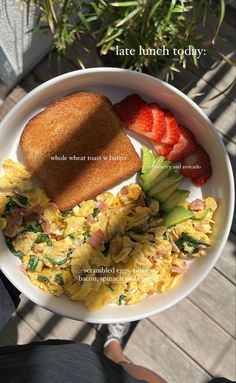 a white plate topped with eggs and toast next to strawberries on top of a wooden table