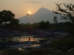 a person standing in the middle of a river at sunset with mountains in the background