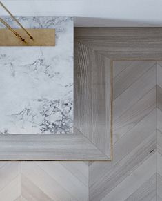 a white marble and gold frame hanging on the wall next to a wooden herringbone floor