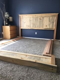 a wooden bed frame in a bedroom with carpeted flooring and blue walls behind it