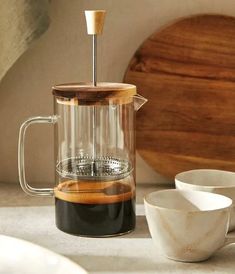 a glass coffee maker sitting on top of a counter next to two bowls and a wooden cutting board