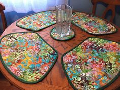 four placemats on a wooden table with a vase and glass in the middle