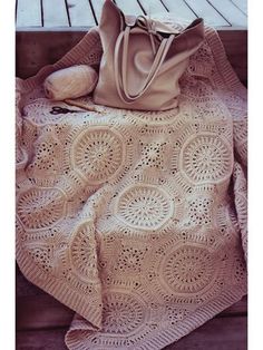 a crocheted blanket and purse sitting on a wooden bench next to a handbag