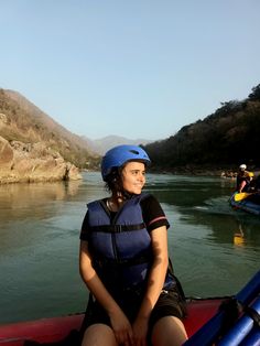 a woman in a blue life jacket and helmet on a boat with mountains in the background