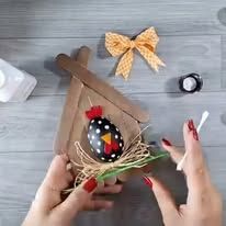 a woman is decorating an easter egg in a house shaped like a chicken on the table