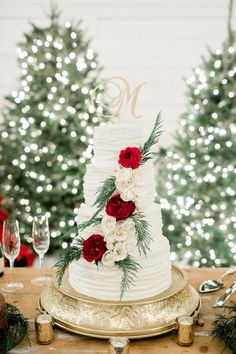 a white wedding cake with red flowers and greenery sits on a gold platter