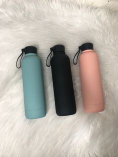 three different colored water bottles sitting next to each other on a white furnishing