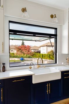 an open kitchen window with blue cabinets and white counter tops in front of the sink