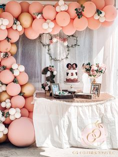 the dessert table is set up with pink and gold balloons, white flowers, and greenery