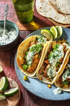 three tacos on a plate with limes, sour cream and cilantro