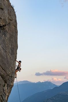 a man climbing up the side of a mountain with a rope attached to his back