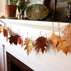 autumn leaves are hung on a mantle in front of a fireplace