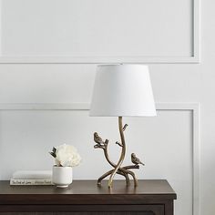 a table with a lamp and flowers on it next to a white vase filled with flowers