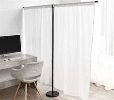 a desk with a computer on it next to a white curtained wall and chair