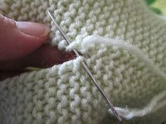 someone is stitching the stitches on a white knitted sweater with scissors in their left hand