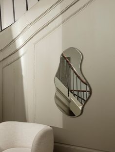 a mirror hanging on the side of a wall next to a white chair and stair case