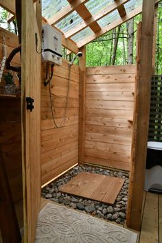 a shower in a wooden enclosure surrounded by rocks and wood planks, with a white rug on the floor