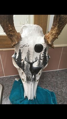 a deer skull with antlers and trees painted on it's face is sitting on a blue towel