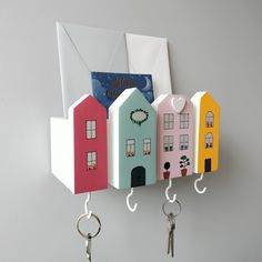 three houses are hanging from hooks on the wall with keys in front of them and an envelope behind them