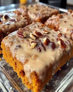 several pieces of cake with frosting and nuts on top sitting in a glass dish