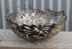 a metal bowl sitting on top of a wooden table filled with lots of different types of keys