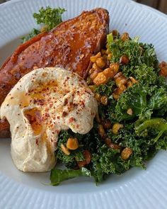 a white plate topped with meat covered in sauce next to a pile of greens and nuts