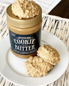 two cookies on a plate next to a jar of peanut butter sitting on a wicker place mat