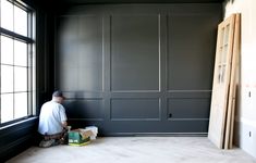 a man is painting the walls of a room with dark gray paint and white trim