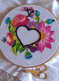 an embroidered heart surrounded by flowers on a white surface with scissors and thread next to it