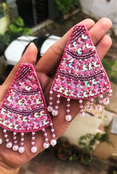 two pink and green earrings in the palm of someone's hand, with beads hanging from them