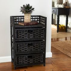 a black wicker side table with two drawers and a potted plant on top