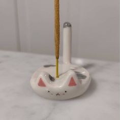 a white cat toothbrush holder with a yellow tooth brush in it's mouth