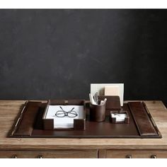 a wooden desk topped with a brown tray and office supplies on top of it next to a black wall