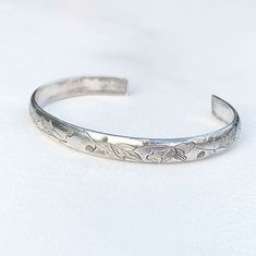 The listing is for an Antique Chinese Silver Cuff Bracelet. It features an engraved floral motif design. There cuff is beautifully decorated with flowers, leaves and buds covering the whole cuff which is made with half round wire. The cuff is made with old silver that shows patina. These bracelets where part of a pair worn by Chinese brides; sometimes called Wedding Cuffs. Weight: 13.3 grams Marks: Signed with Chinese Characters. Tests as silver. Measurements: It measures approximately 5 1/8 inc Floral Motif Design, Chinese Bride, Large Cuff Bracelet, Wedding Cuff, Engraved Wedding, Chinese Characters, Turquoise Cuff, Motif Design, Flowers Leaves