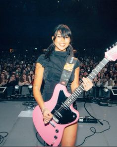 a woman holding a pink guitar in front of an audience