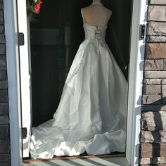 a white wedding dress is on display in the door to a brick building with flowers hanging from it