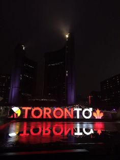 the toronto sign is lit up at night with lights on it and buildings in the background