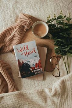 a cup of coffee next to a book on a bed with a scarf and eyeglasses