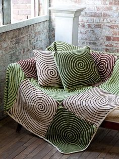 a couch with four pillows on top of it in front of a brick wall and window