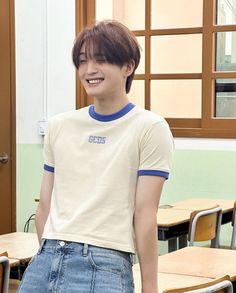 a young man standing in front of desks with his hand on his hip and smiling at the camera