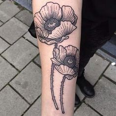 a black and white tattoo with three flowers on the left arm, in front of a brick walkway