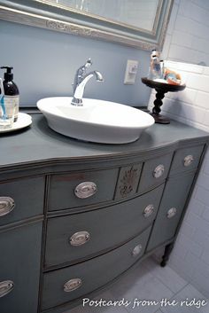 a bathroom sink sitting on top of a gray dresser