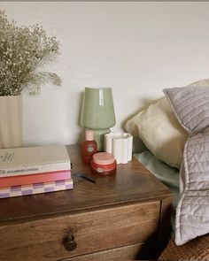 a wooden dresser topped with books and vases next to a pillow on top of a bed