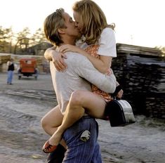 black and white photograph of two people kissing each other on the street with logs in the background