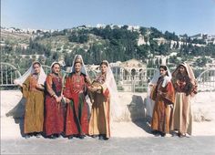 four women dressed in traditional clothing posing for a photo on the side of a hill