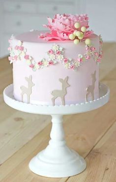 a pink and white cake with flowers on top is sitting on a wooden table in front of a window