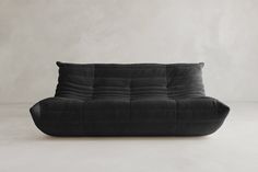 a black couch sitting on top of a white floor next to a gray wall in an empty room