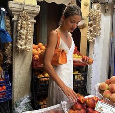 a woman standing in front of a fruit stand with lots of peaches and oranges