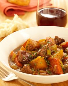 a white bowl filled with stew next to a glass of wine